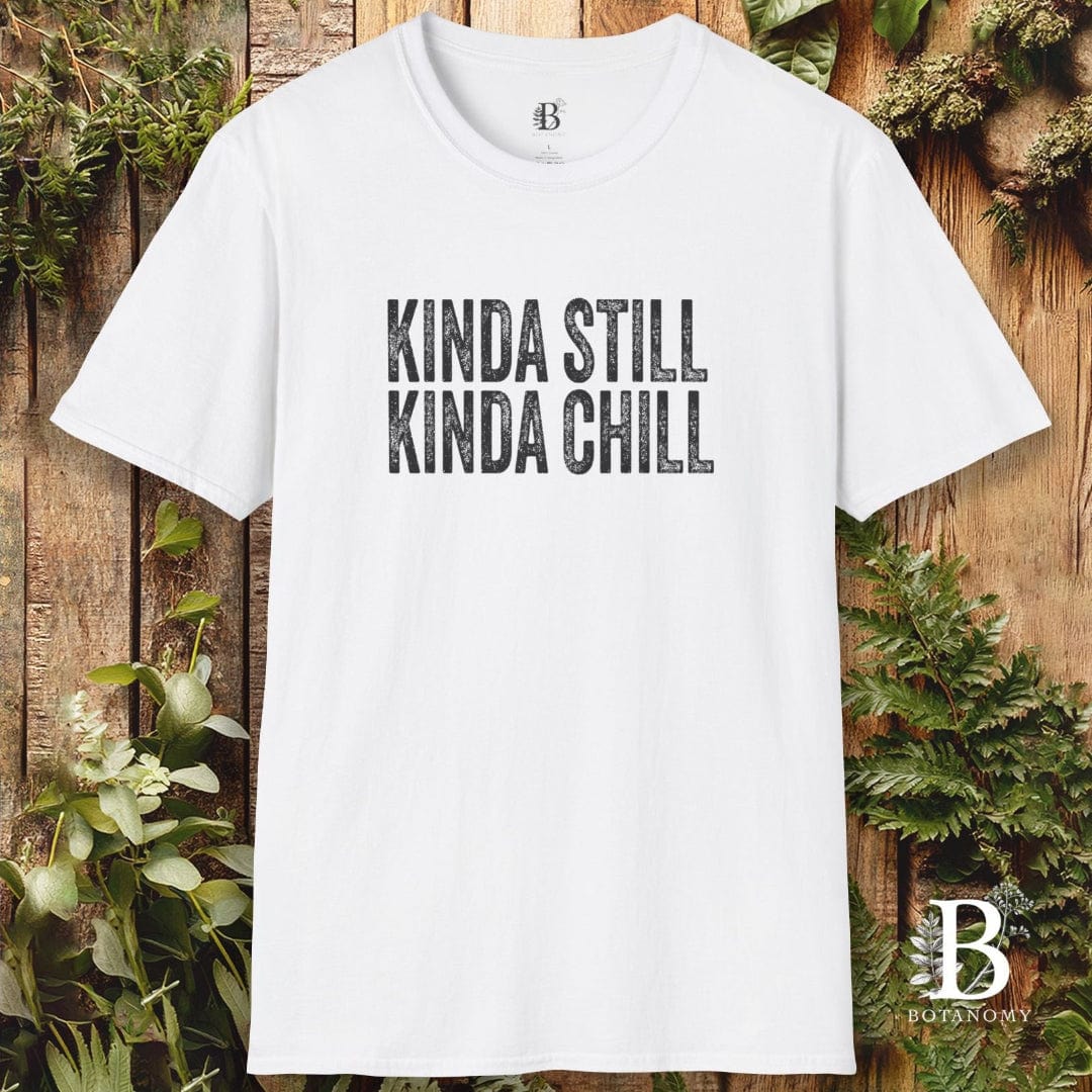 White t-shirt with 'KINDA STILL KINDA CHILL' text on a wooden background with plants