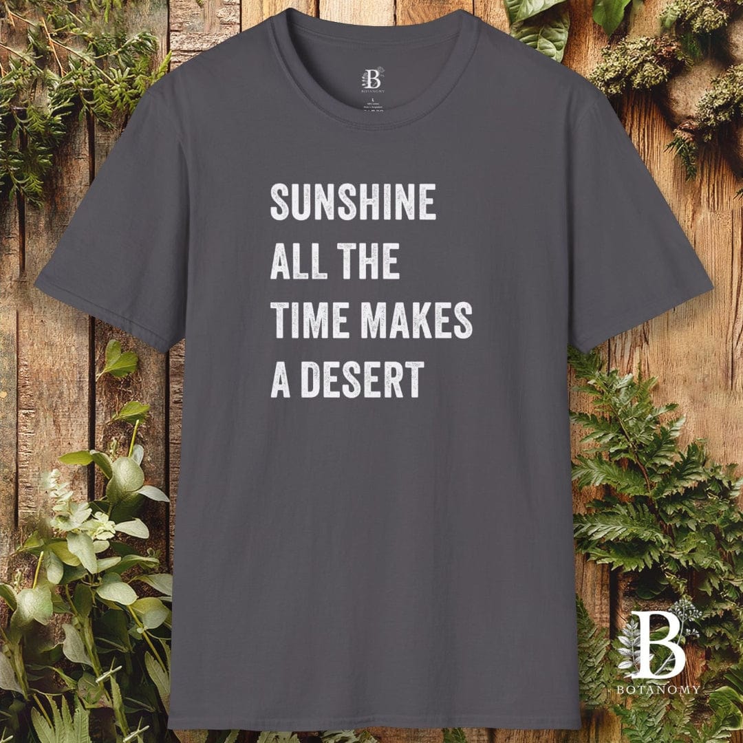 Gray t-shirt with white text 'Sunshine all the time makes a desert' on a wooden background with plants.