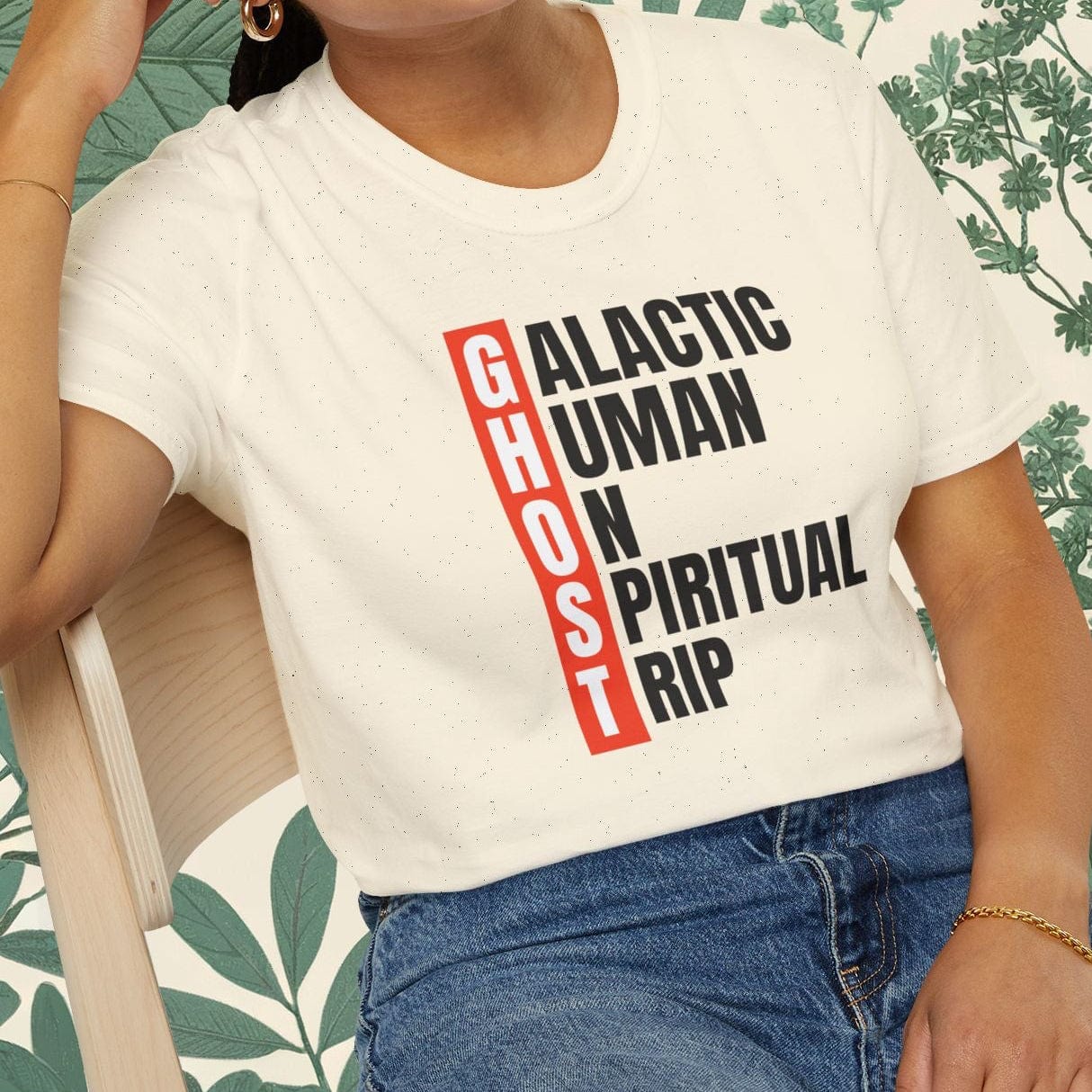Person wearing a white t-shirt with text, sitting on a chair with a floral background