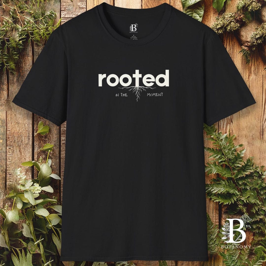 Black t-shirt with 'rooted' text on a wooden background with plants