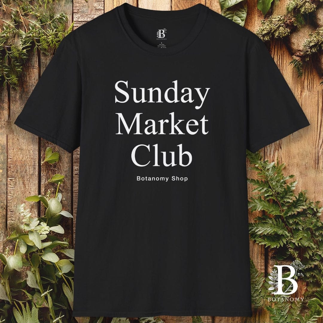 Black t-shirt with 'Sunday Market Club' text on a wooden background with plants