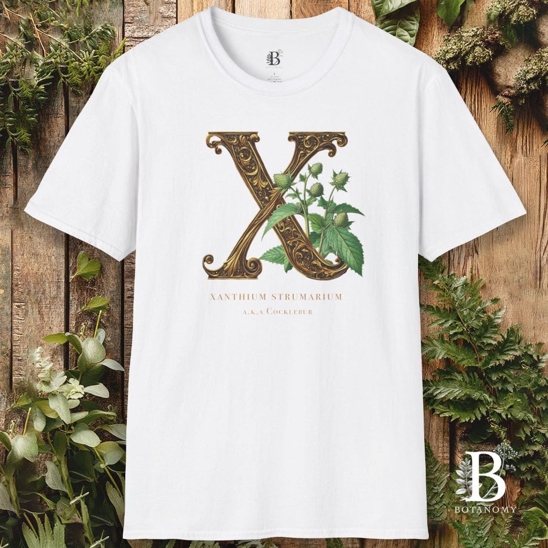 White t-shirt with decorative letter 'X' design on a wooden background with greenery