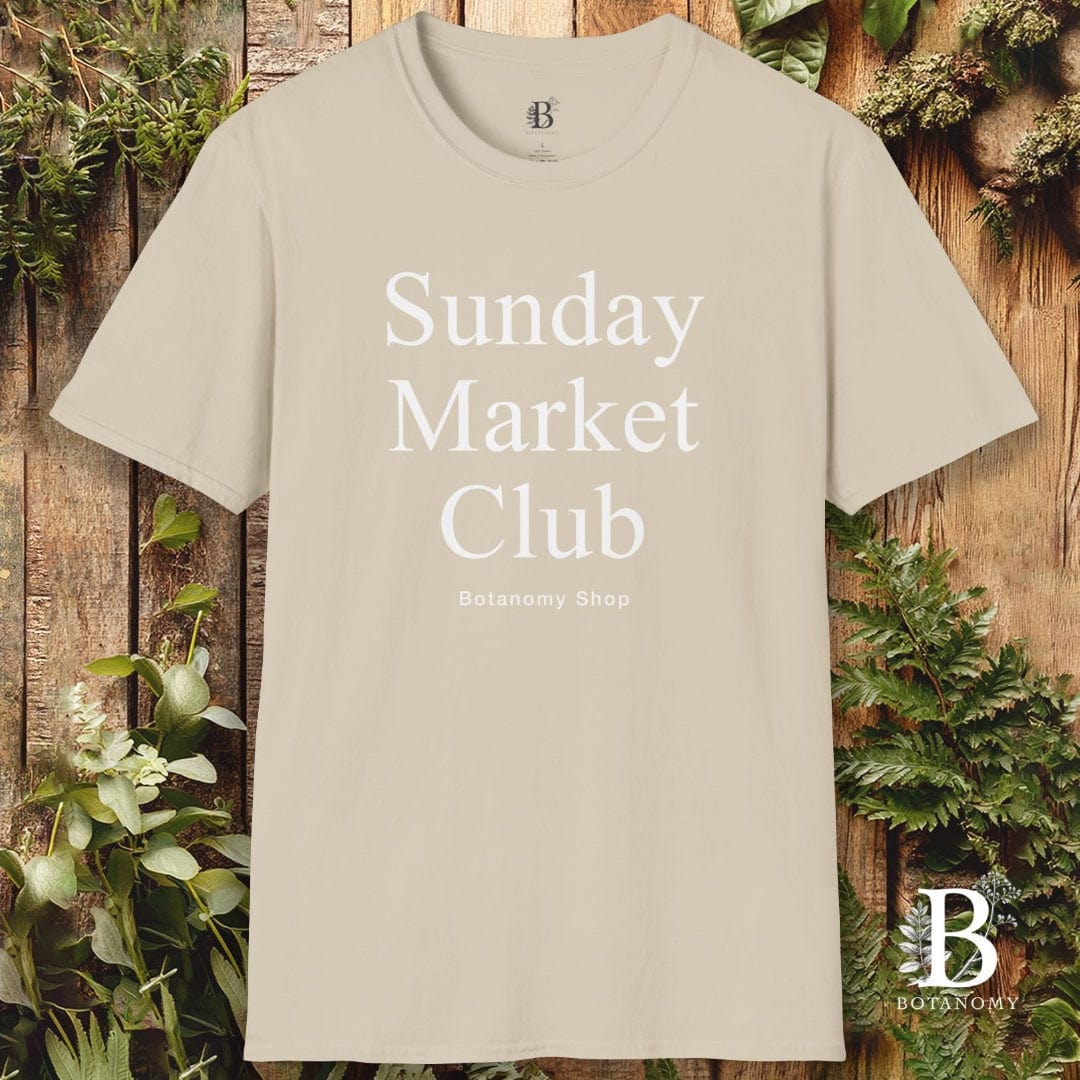 Beige t-shirt with 'Sunday Market Club' text on a wooden background with greenery