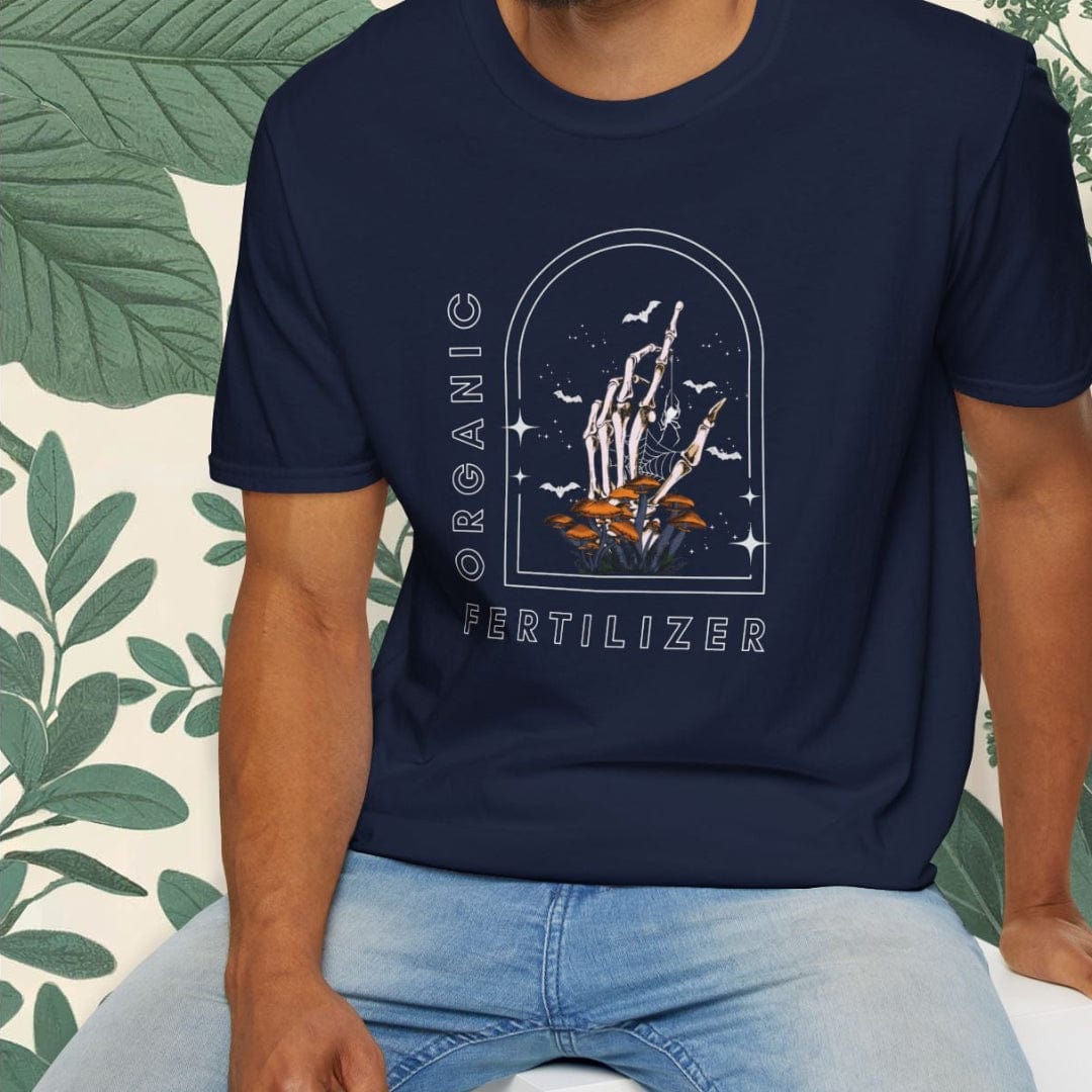 Man wearing a navy blue t-shirt with a graphic design, sitting on a white stool with a green leafy background.