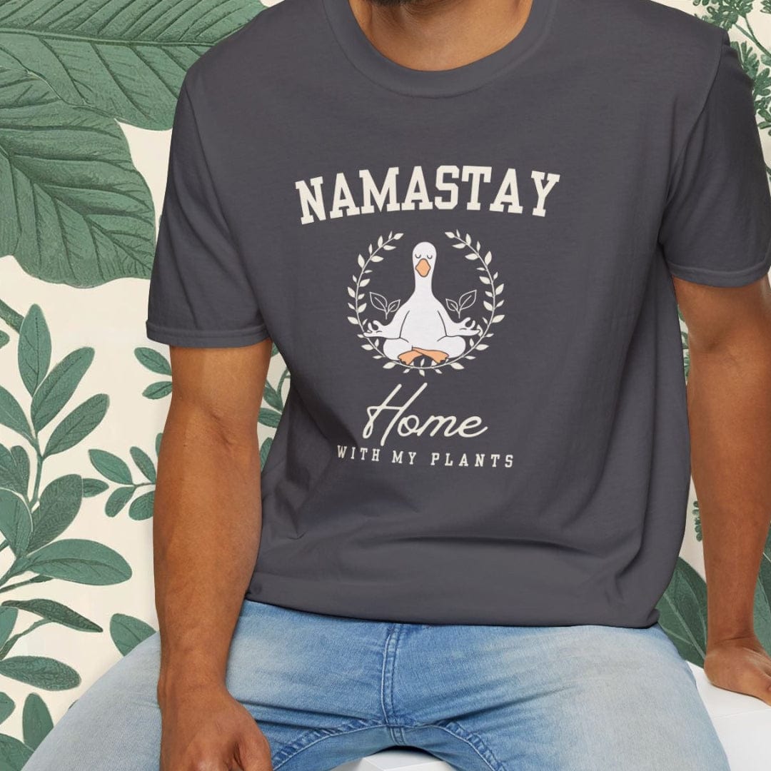 Person wearing a dark gray t-shirt with 'Namastay Home with My Plants' design, sitting against a leafy background.