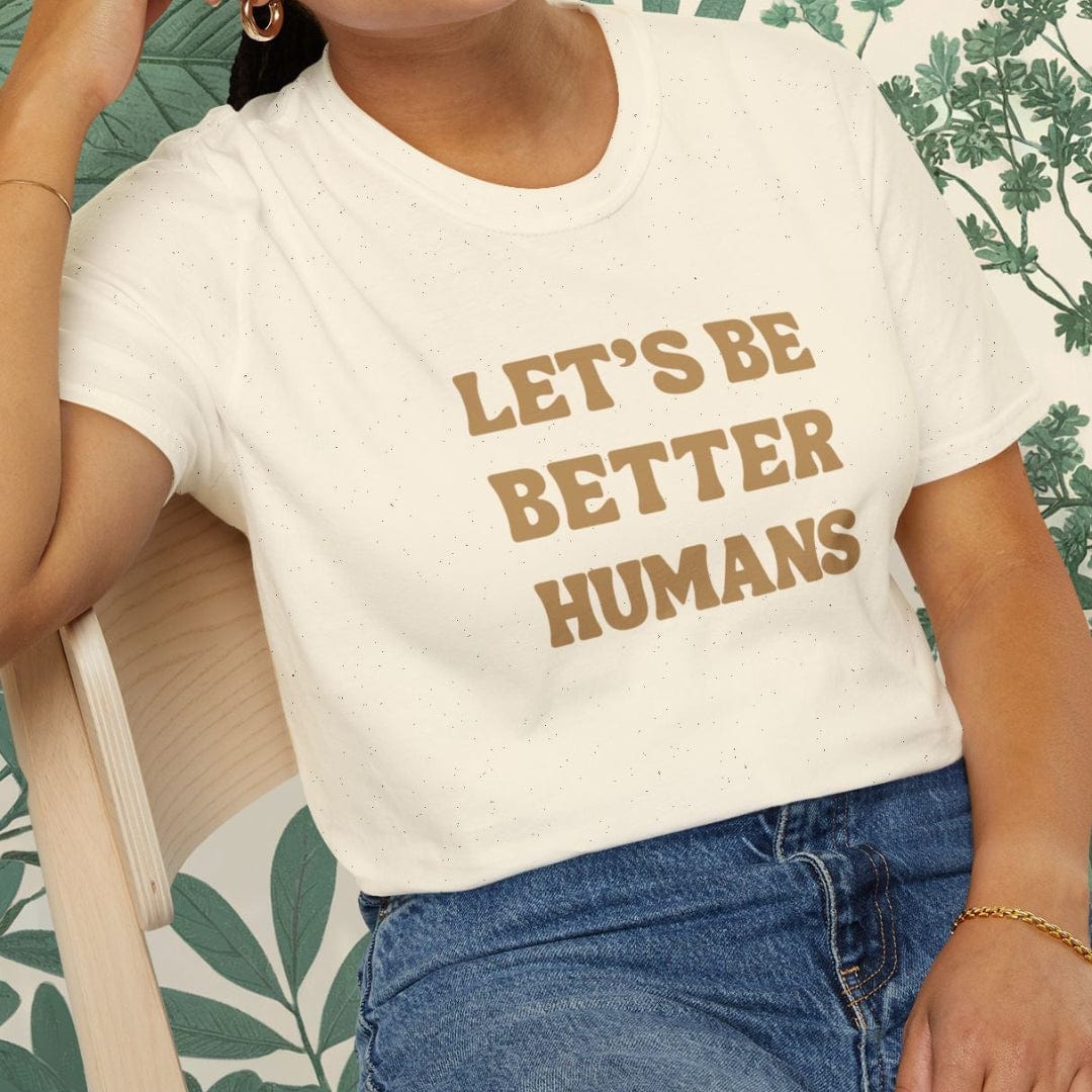 Person wearing a white t-shirt with 'Let's Be Better Humans' text, sitting on a chair.