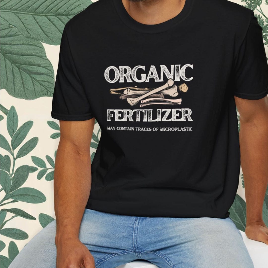 Man wearing a black t-shirt with 'Organic Fertilizer' text, sitting on a white stool with green plants in the background.