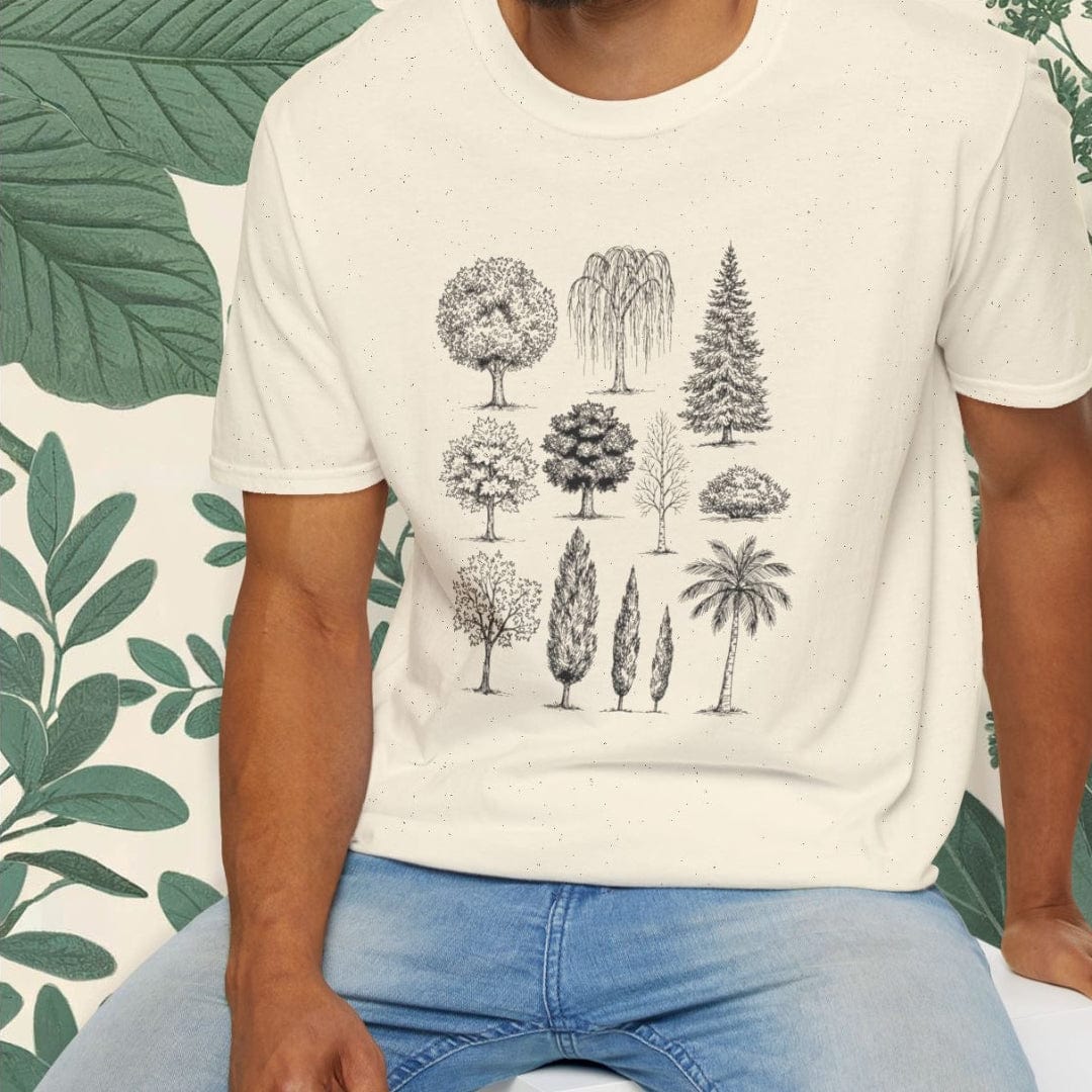 Man wearing a white t-shirt with tree graphics sitting on a white stool against a green leafy background.