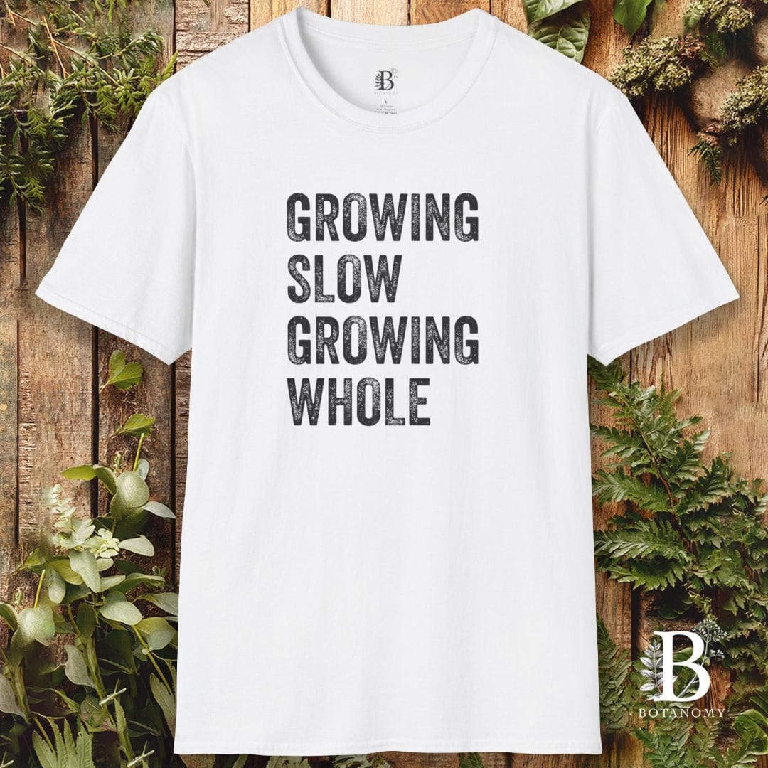 White t-shirt with 'Growing Slow Growing Whole' text on a wooden background with plants.
