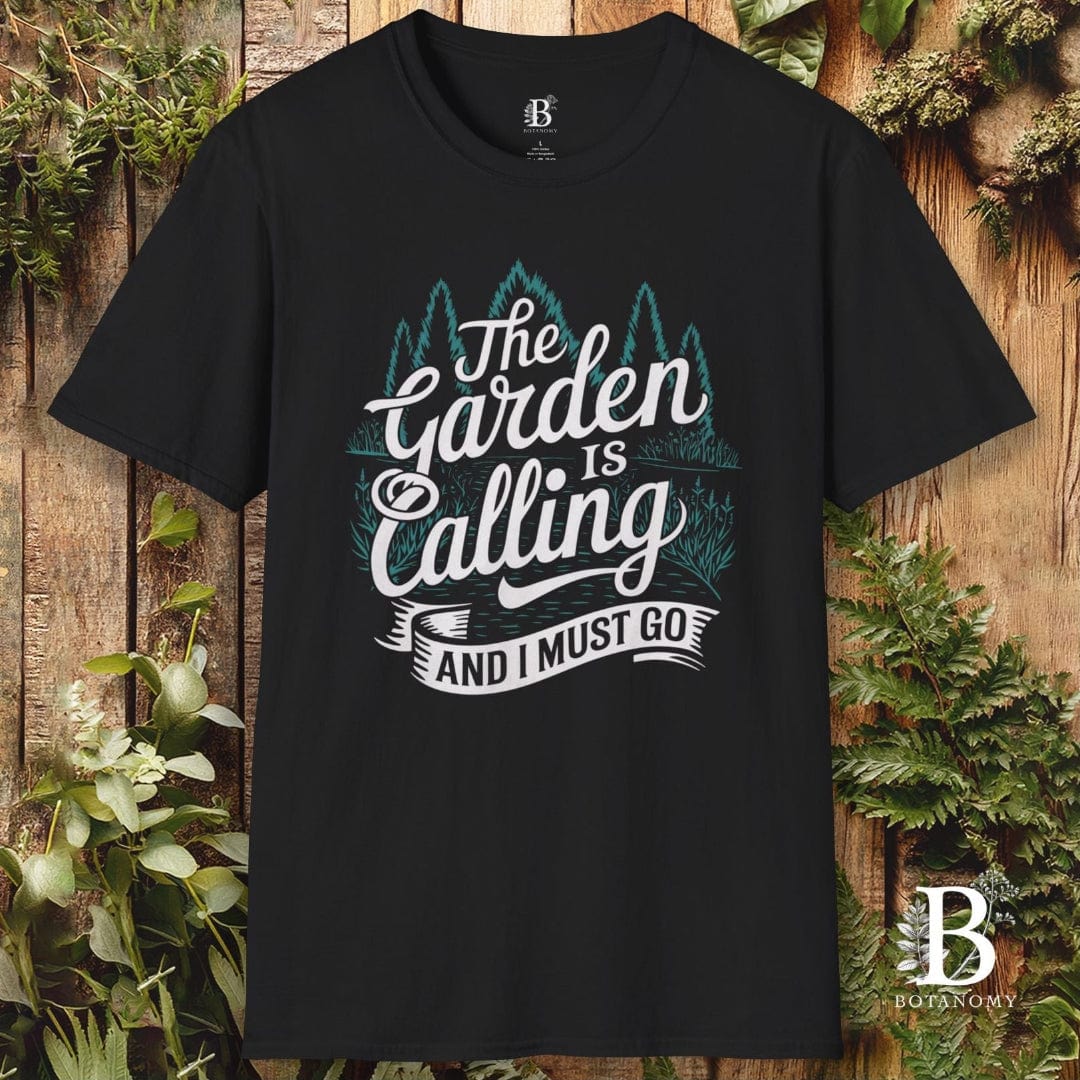 Black t-shirt with 'The Garden is Calling and I Must Go' text and brand logo on a wooden background with plants.