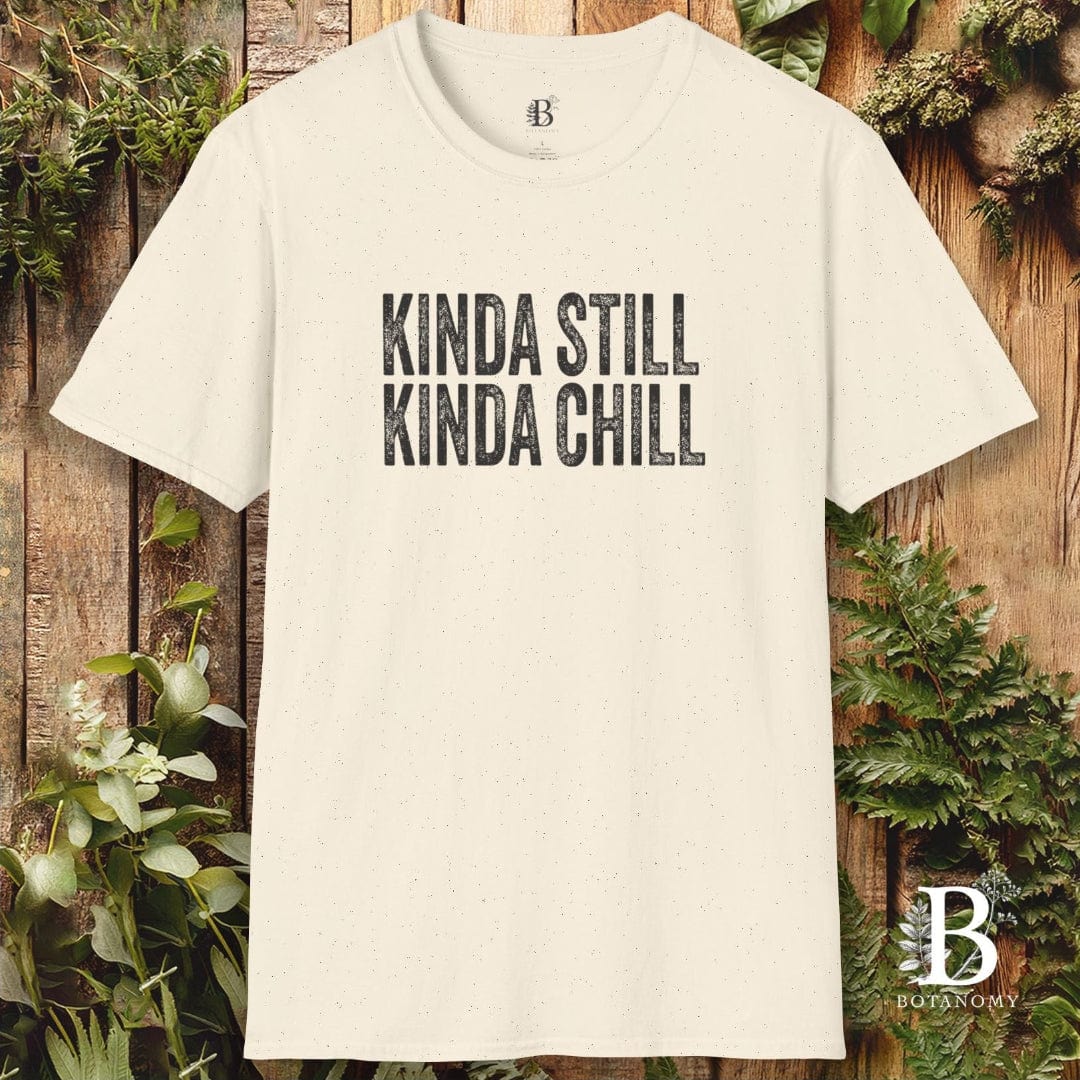 Beige t-shirt with 'KINDA STILL KINDA CHILL' text on a wooden background with greenery