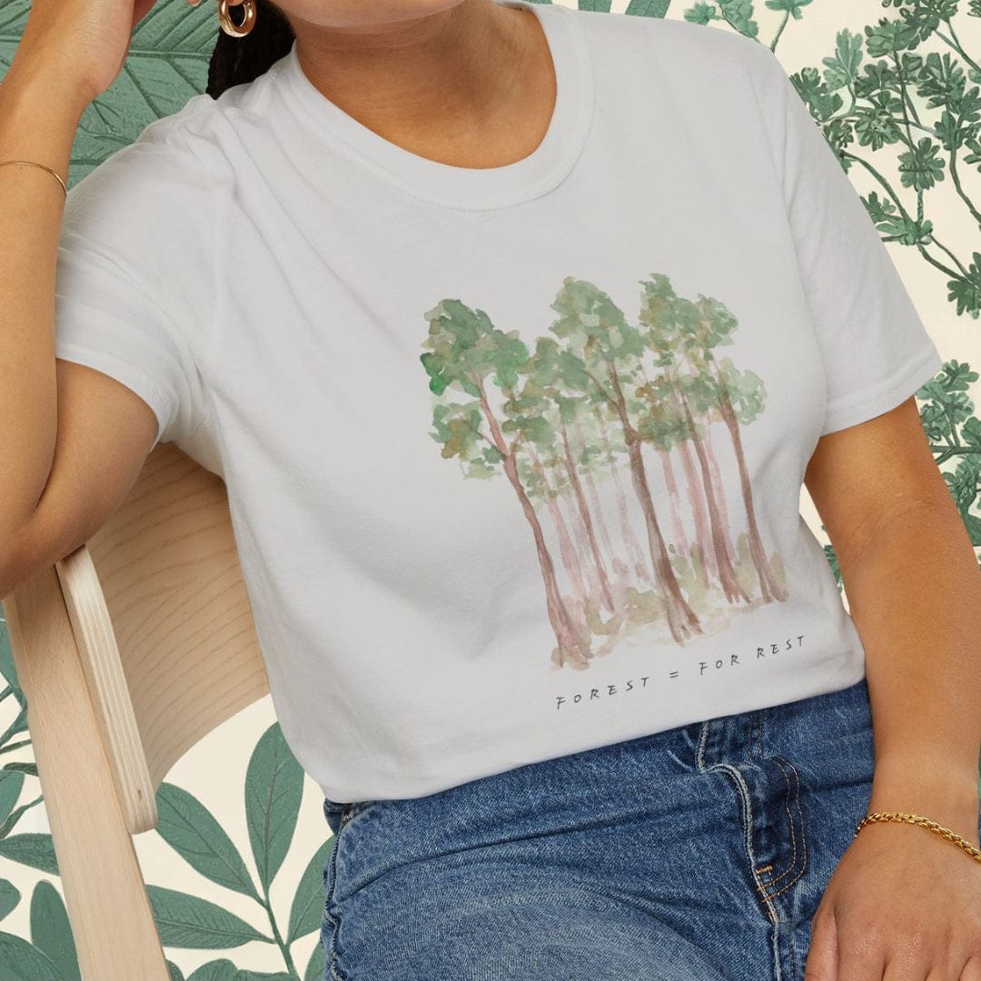 Woman wearing a white t-shirt with a forest graphic and blue jeans, sitting on a chair.