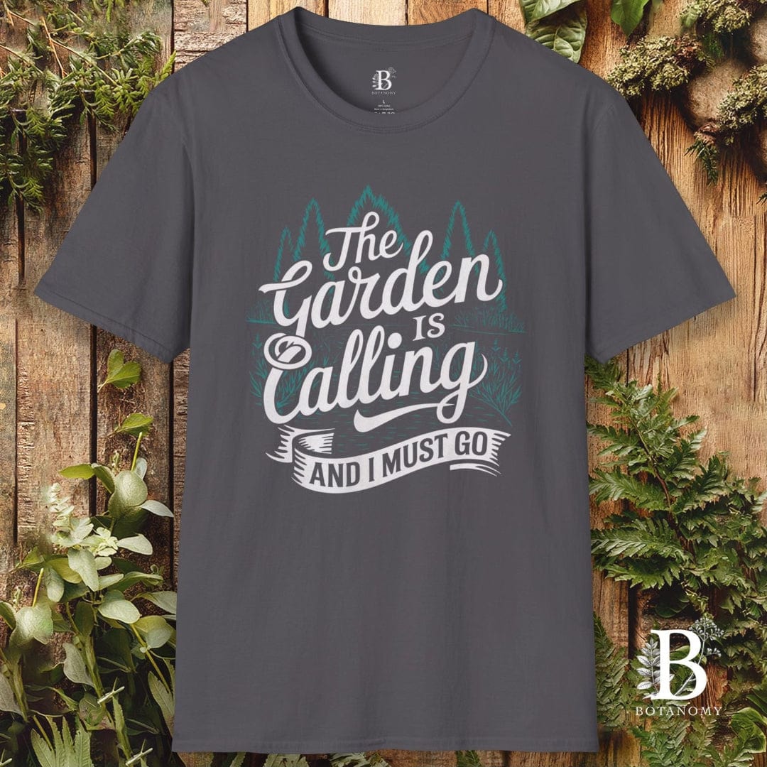 Gray t-shirt with 'The Garden is Calling' text on a wooden background with plants
