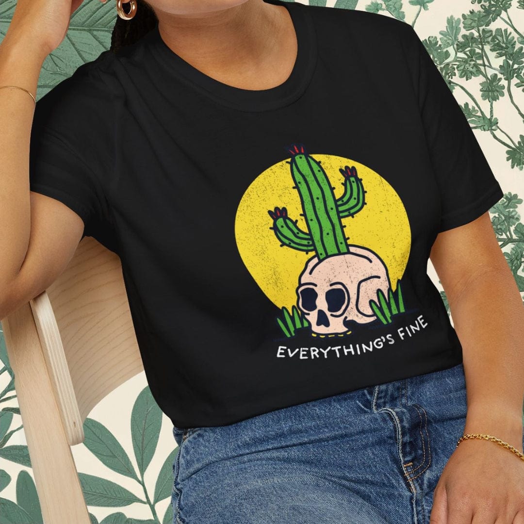 Person wearing a black t-shirt with a cactus and skull design, sitting on a chair.