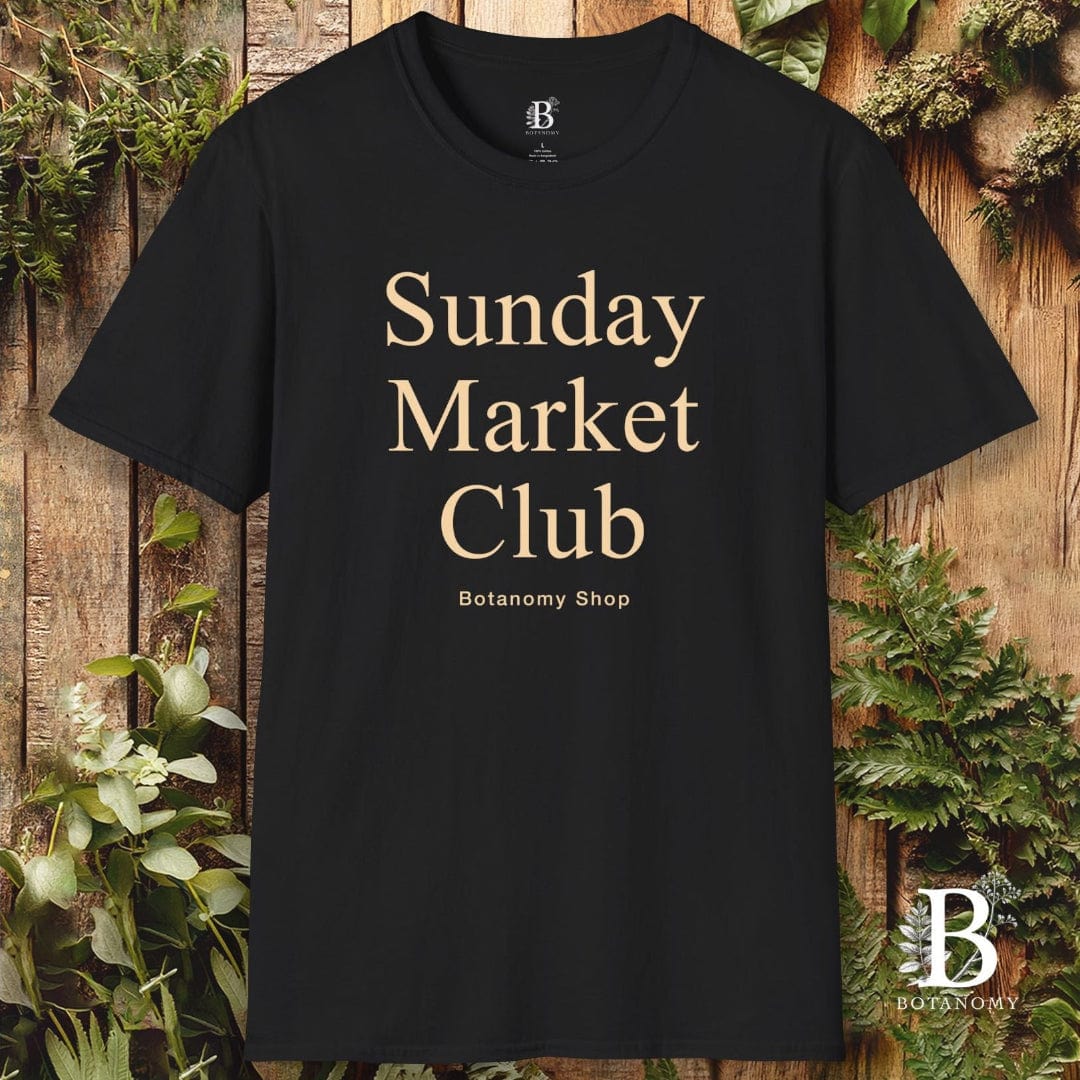 Black t-shirt with 'Sunday Market Club' text on a wooden background with plants