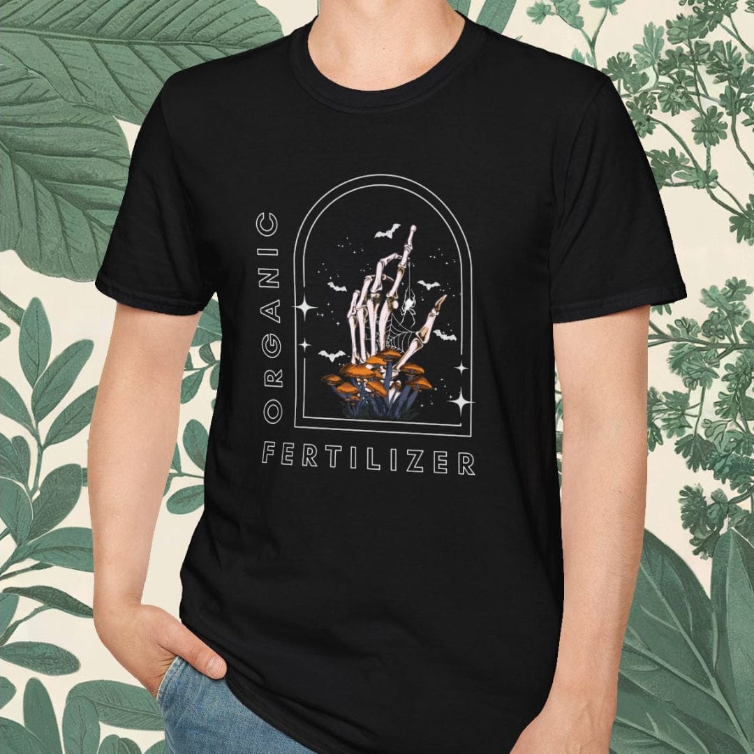 Person wearing a black t-shirt with graphic design and text, standing against a leafy background