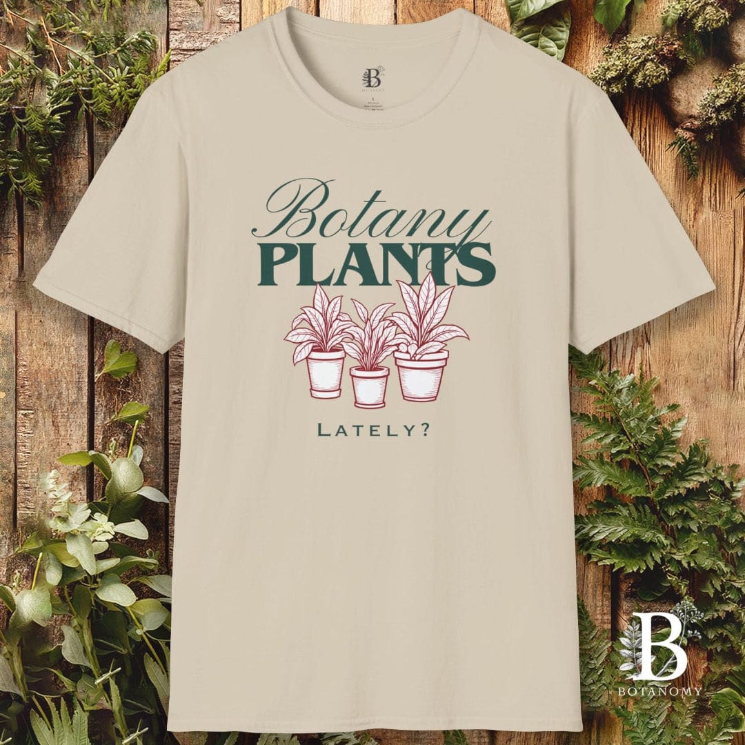 Beige t-shirt with 'Botany Plants Lately?' design on a wooden background with plants.