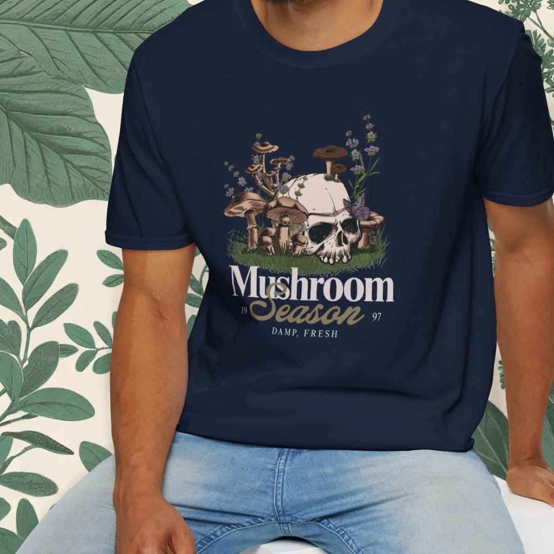 Man wearing a navy blue t-shirt with 'Mushroom Season' graphic design, sitting on a white stool.