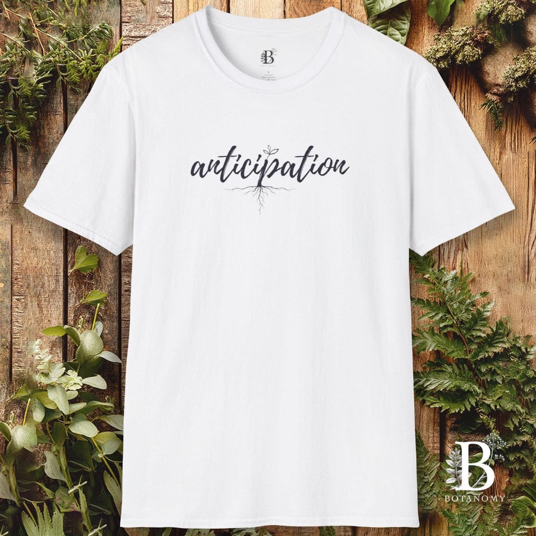White t-shirt with 'anticipation' text on a wooden background with greenery