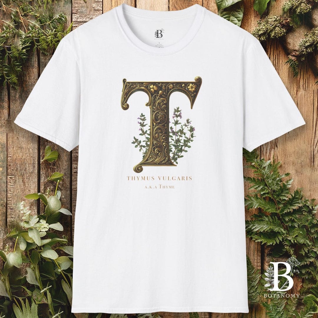 White t-shirt with decorative letter 'T' design on a wooden background with plants