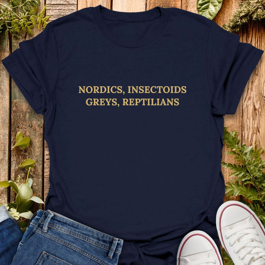 Navy blue t-shirt with gold text 'NORDICS, INSECTOID斯 GREYS, REPTILIAN斯' on a wooden surface with plants.