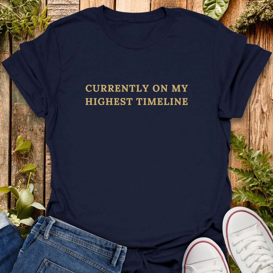 Navy blue t-shirt with 'Currently on my highest timeline' text on a wooden surface with plants, jeans and sneakers.