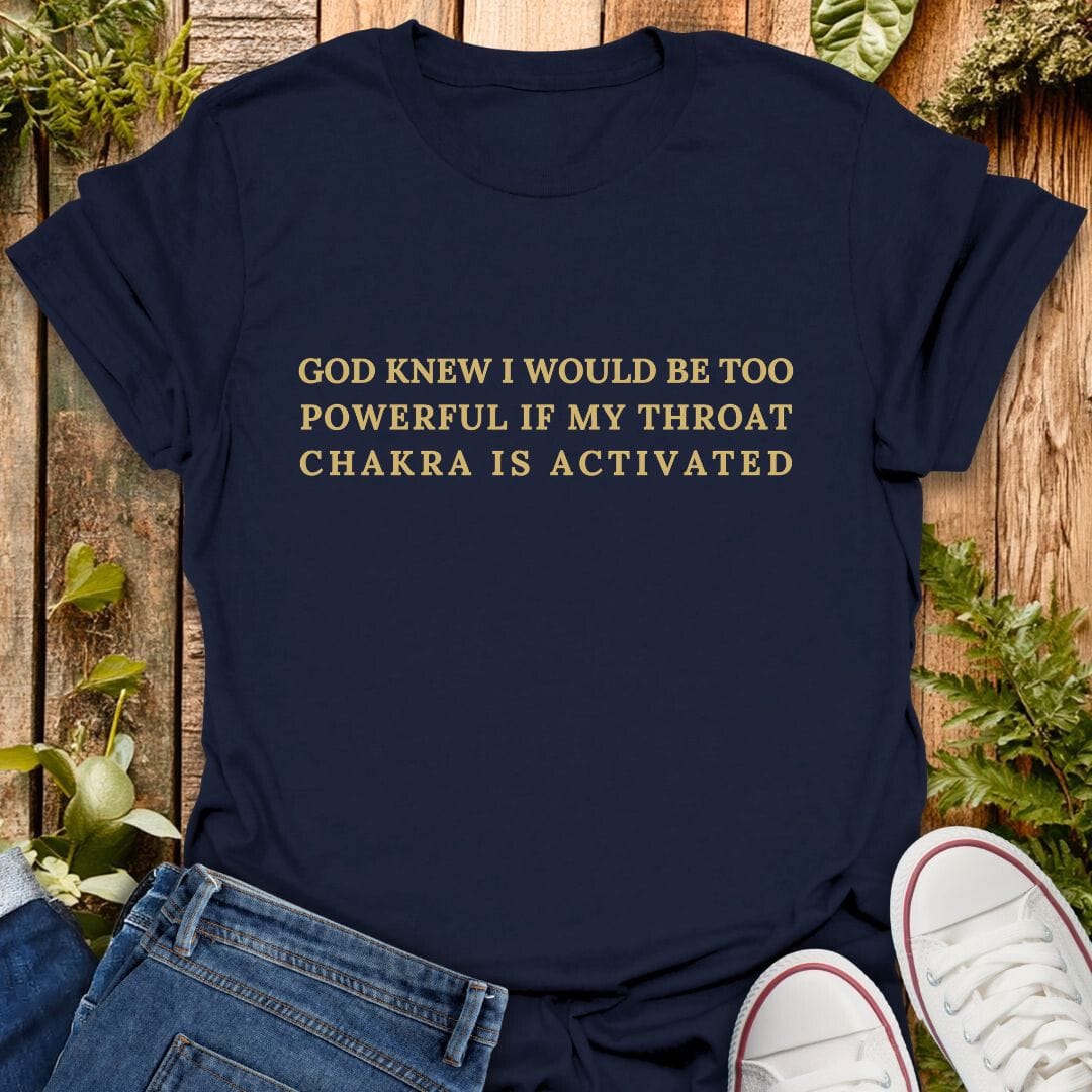 Navy blue t-shirt with "God knew I would be too powerful if my throat chakra is activated" text on a wooden background with plants, jeans, and sneakers.
