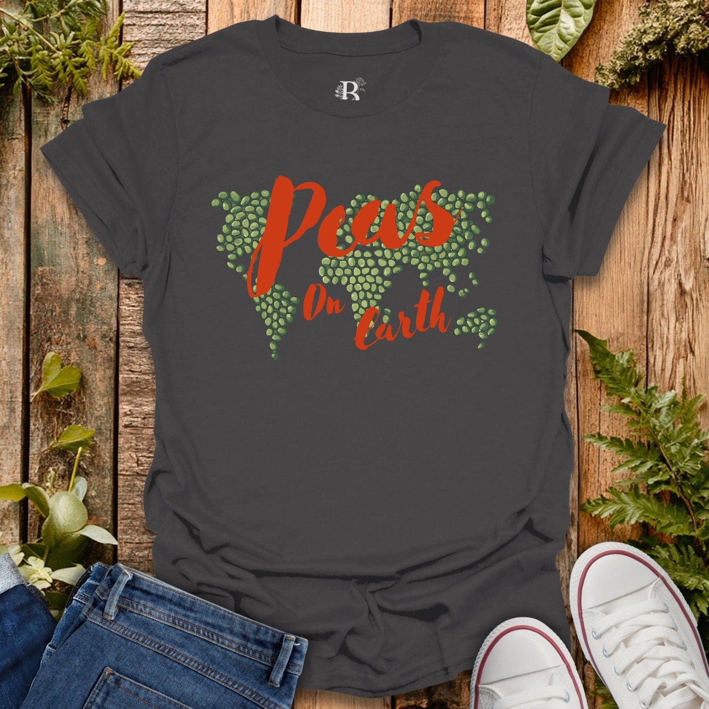 Black t-shirt with 'Peas on Earth' design on a wooden surface with jeans and sneakers.