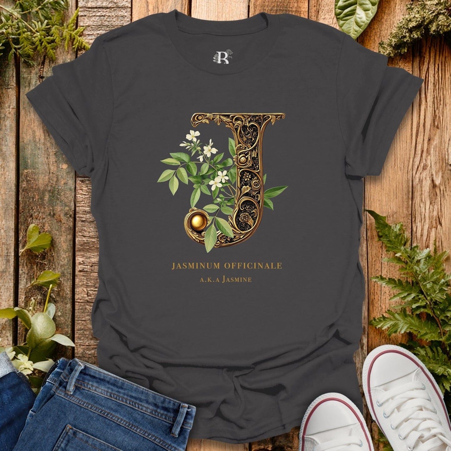 Dark gray t-shirt with decorative letter 'J' design on a wooden surface with plants.