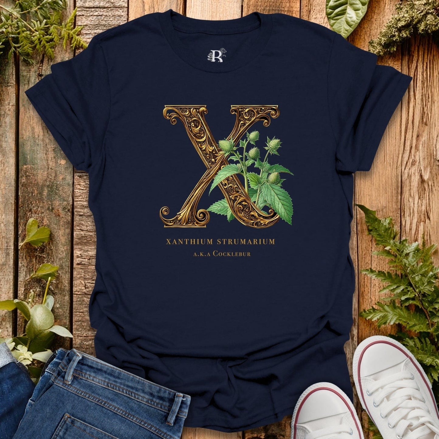 Navy blue t-shirt with gold letter 'X' and plant design on a wooden surface with plants.