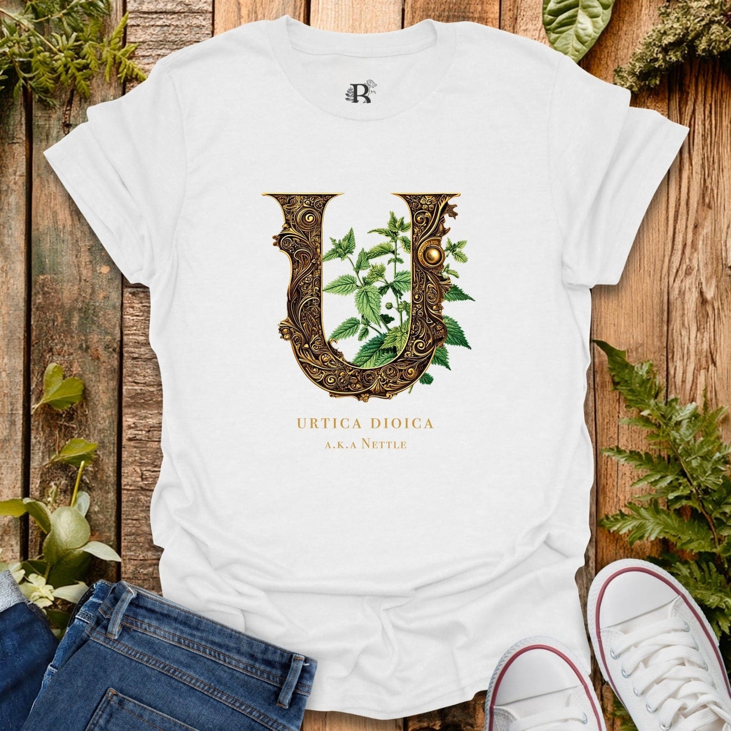 White t-shirt with decorative letter 'U' design featuring plants on a wooden surface with plants around.