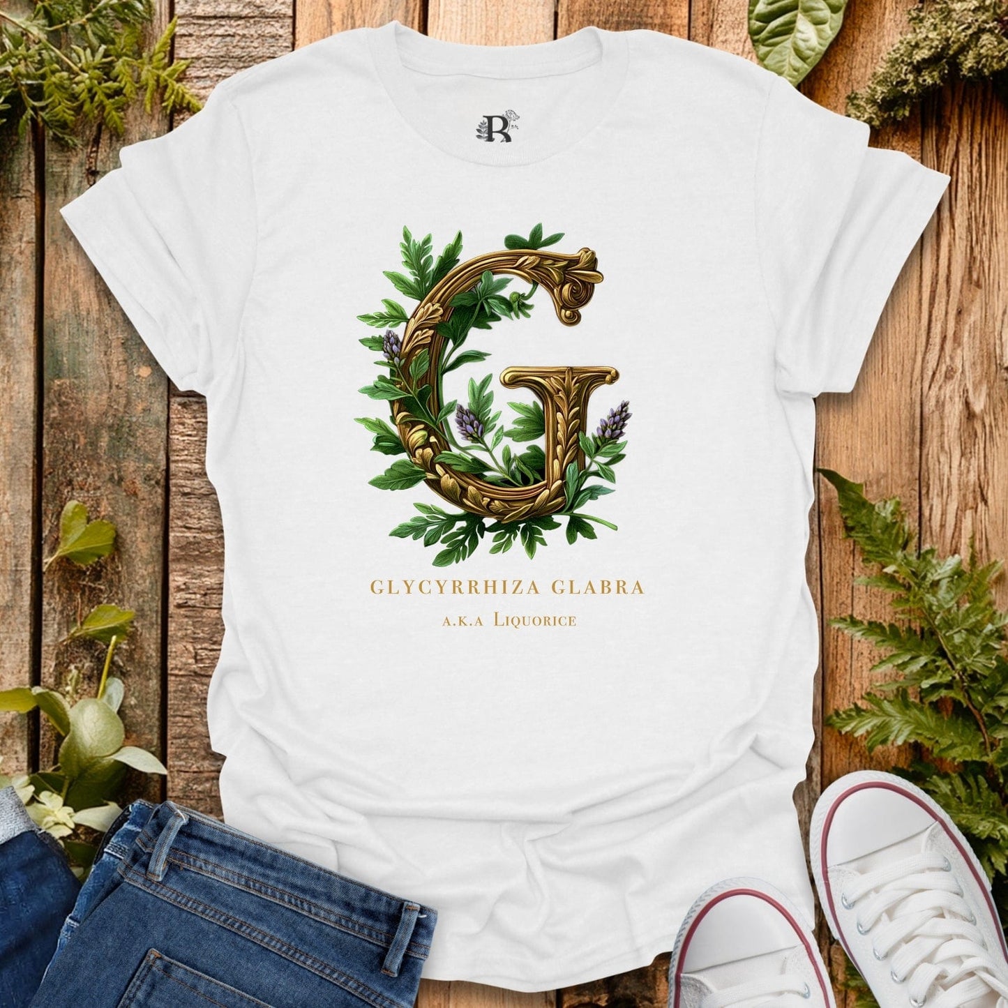 White t-shirt with decorative letter 'G' design on a wooden surface with plants.