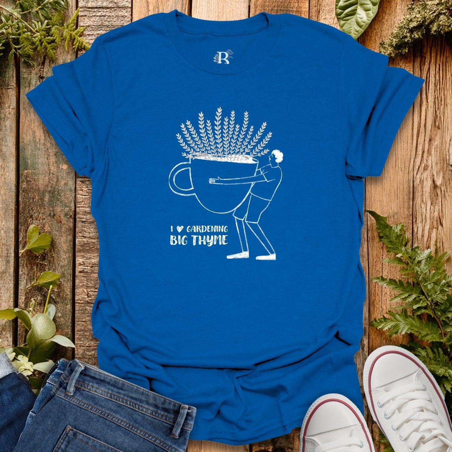 Blue t-shirt with white graphic design on a wooden surface with plants.