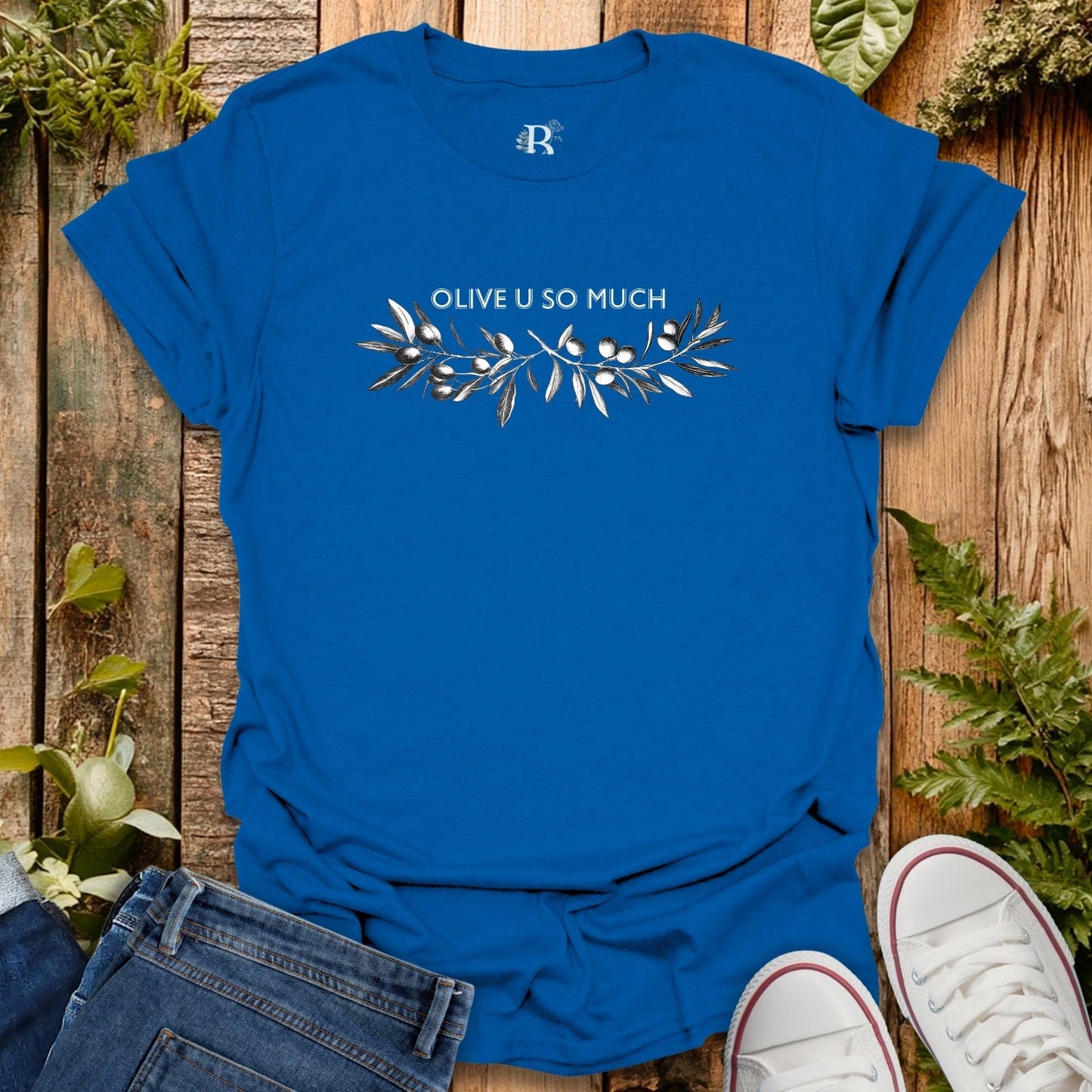Blue t-shirt with 'OLIVE U SO MUCH' design on a wooden background with plants.