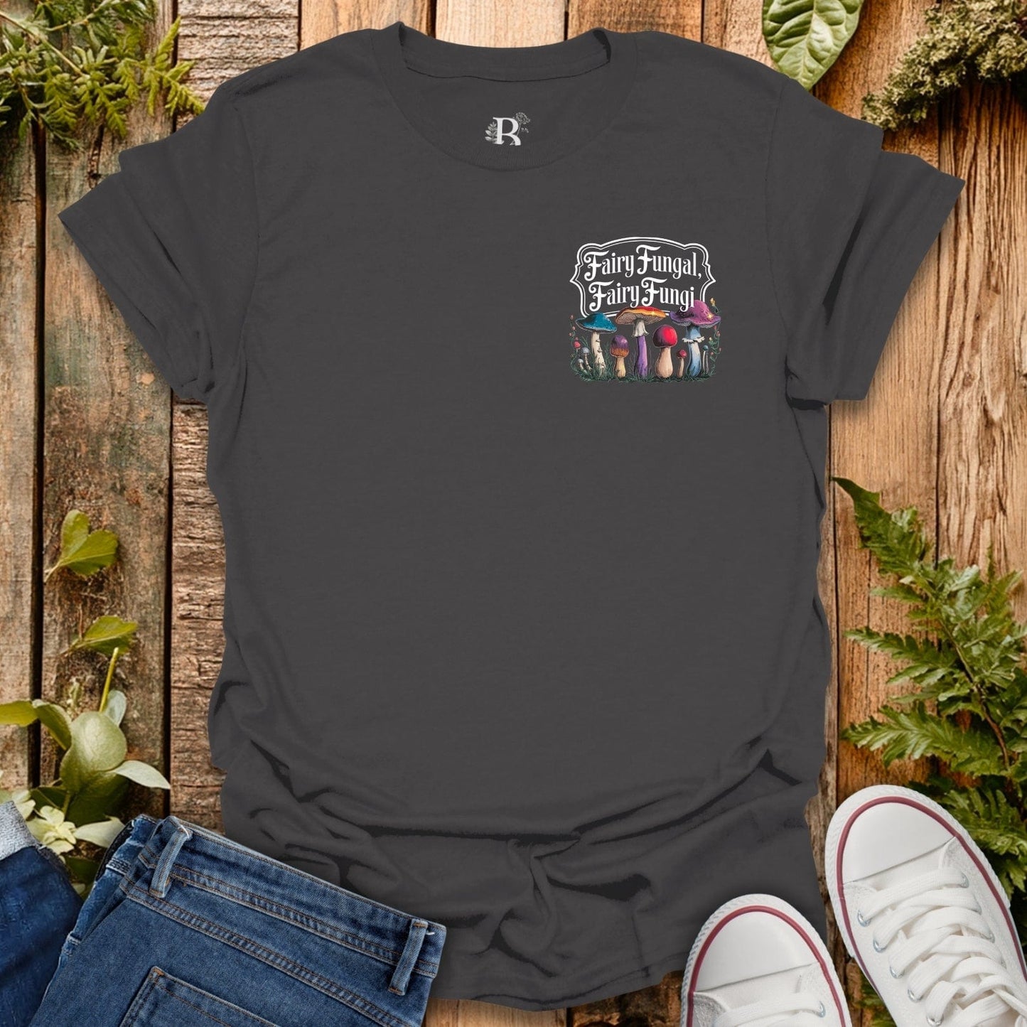 Black t-shirt with 'Fairy Fungal' design on a wooden surface with plants.