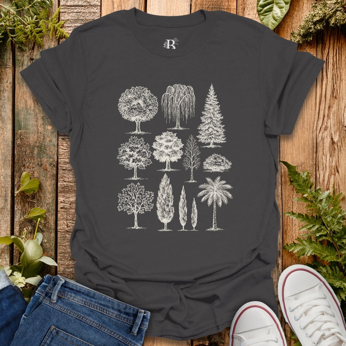 Dark gray t-shirt with white tree illustrations on a wooden surface with plants.