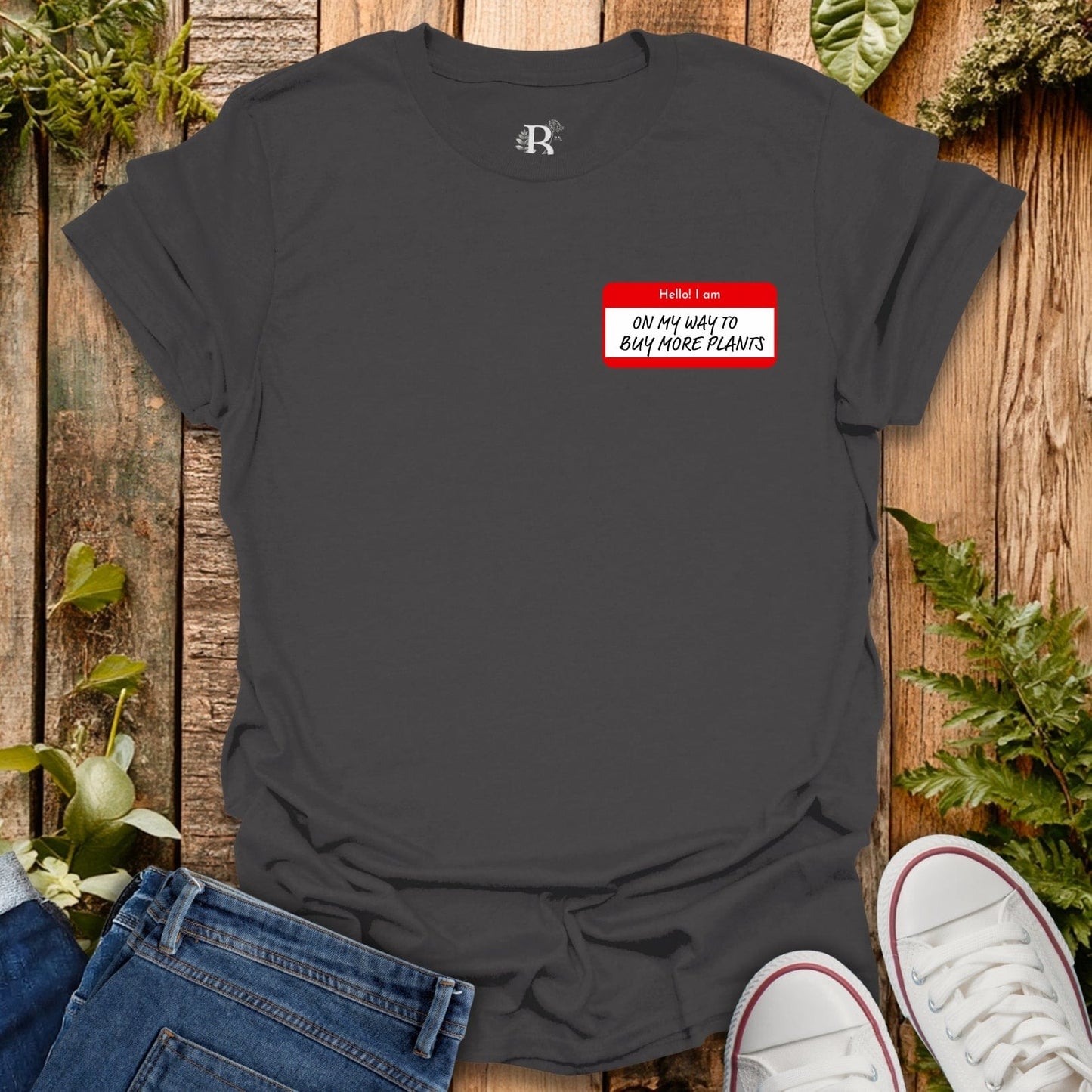 Black t-shirt with a red name tag graphic on a wooden surface with plants.