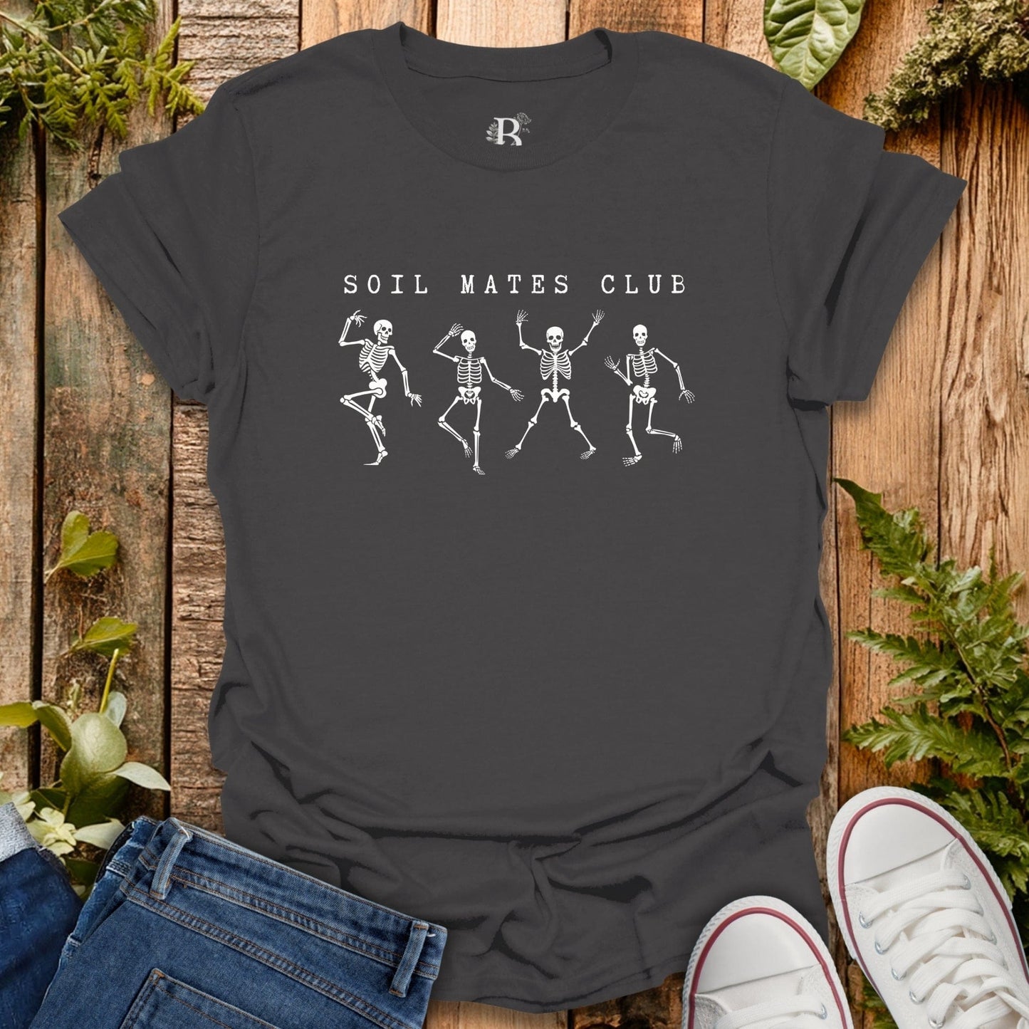 Black t-shirt with 'Soil Mates Club' design on a wooden surface with jeans and sneakers.