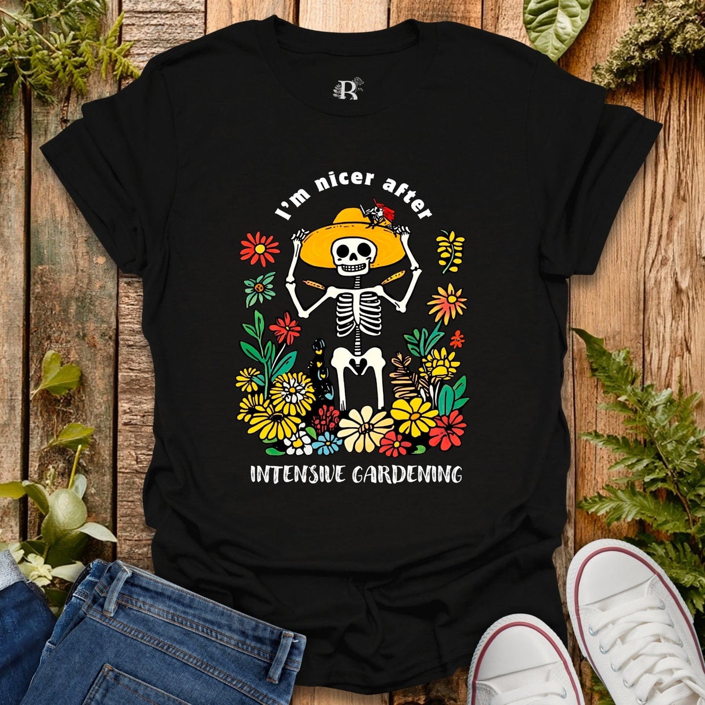 Black t-shirt with skeleton and floral design on a wooden surface with plants.