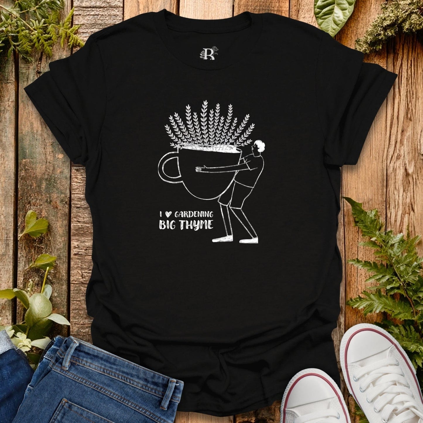 Black t-shirt with white graphic design on a wooden surface with plants.