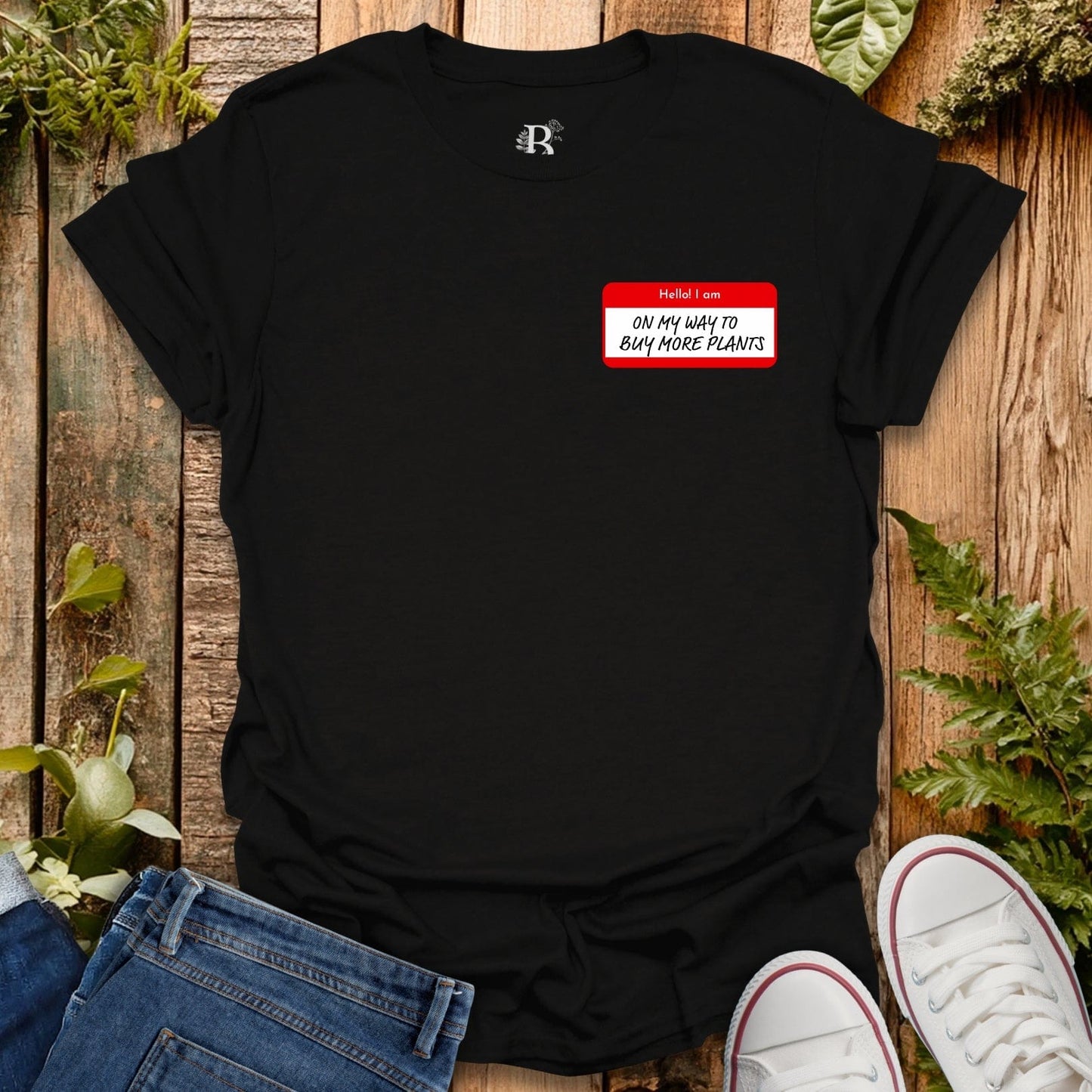 Black t-shirt with a red name tag graphic on a wooden surface with plants.