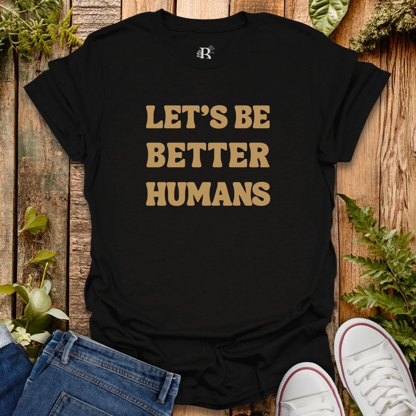 Black t-shirt with 'LET'S BE BETTER HUMANS' text on a wooden surface with jeans and sneakers.
