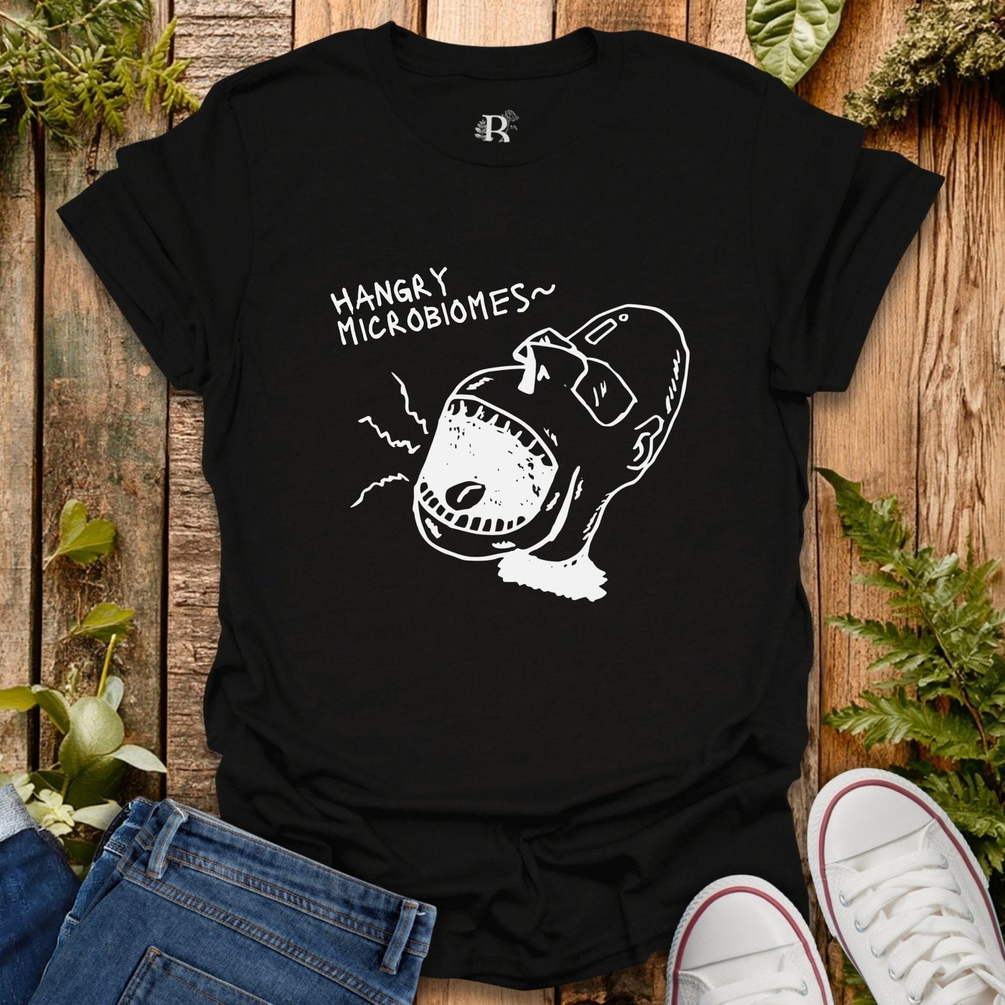 Black t-shirt with a graphic design and text on a wooden surface with plants.