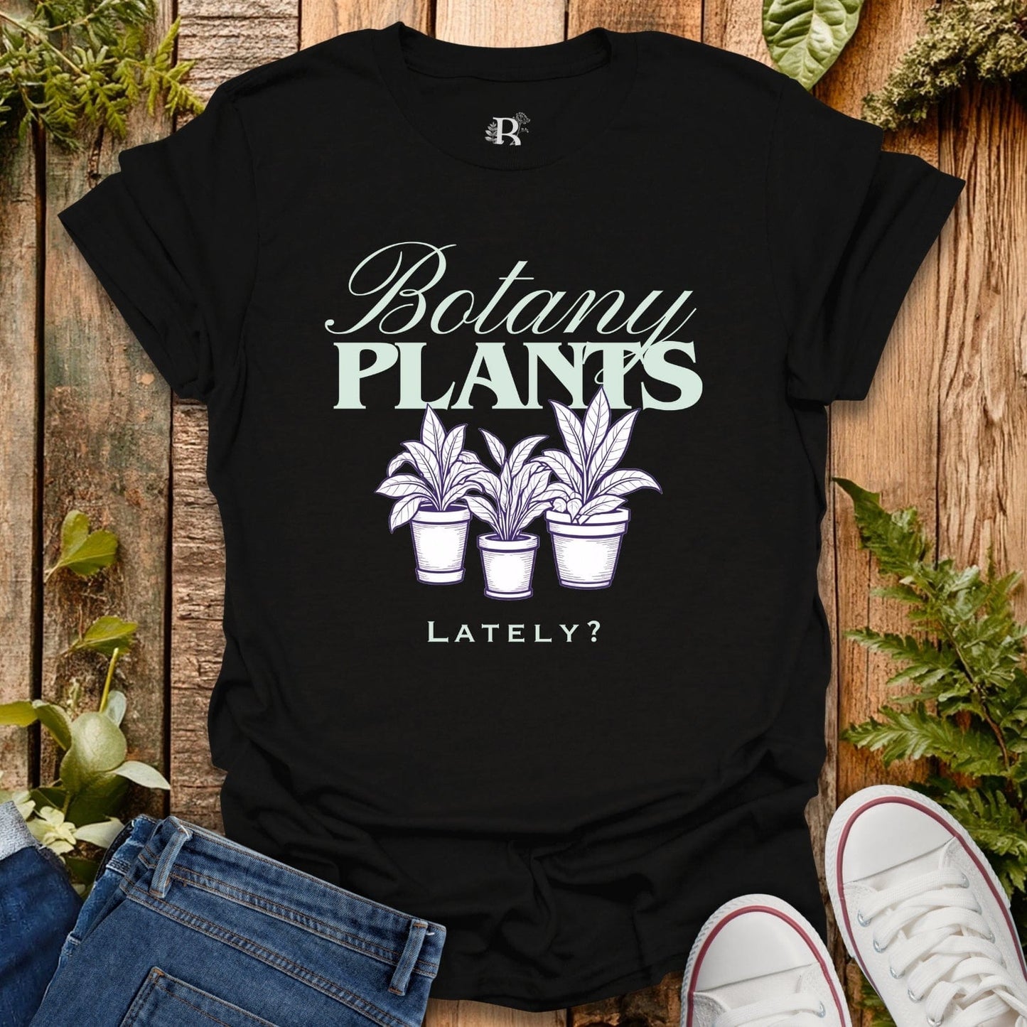 Black t-shirt with 'Botany Plants Lately?' design on a wooden surface with plants.
