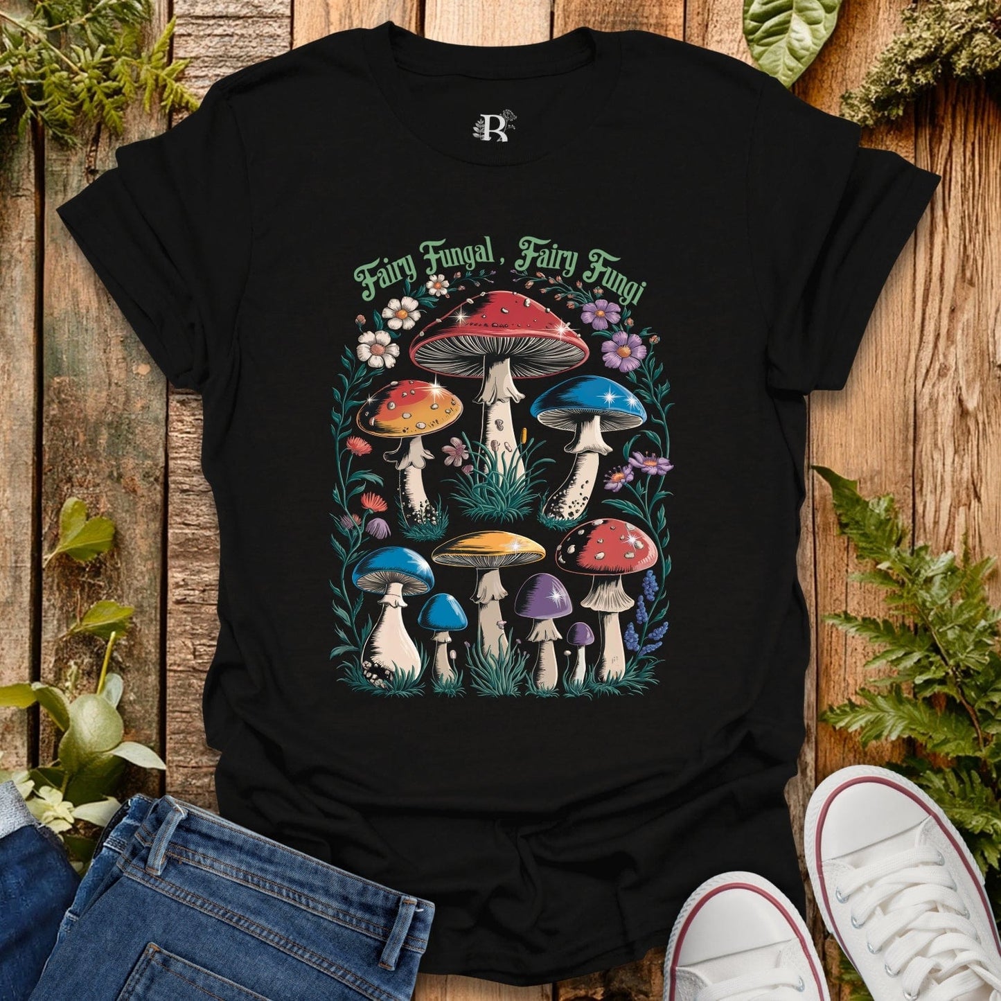 Black t-shirt with colorful mushroom design on a wooden surface with plants.