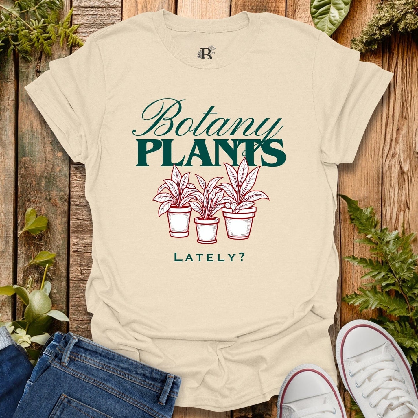 Beige t-shirt with 'Botany Plants Lately?' text and plant illustrations on a wooden background.