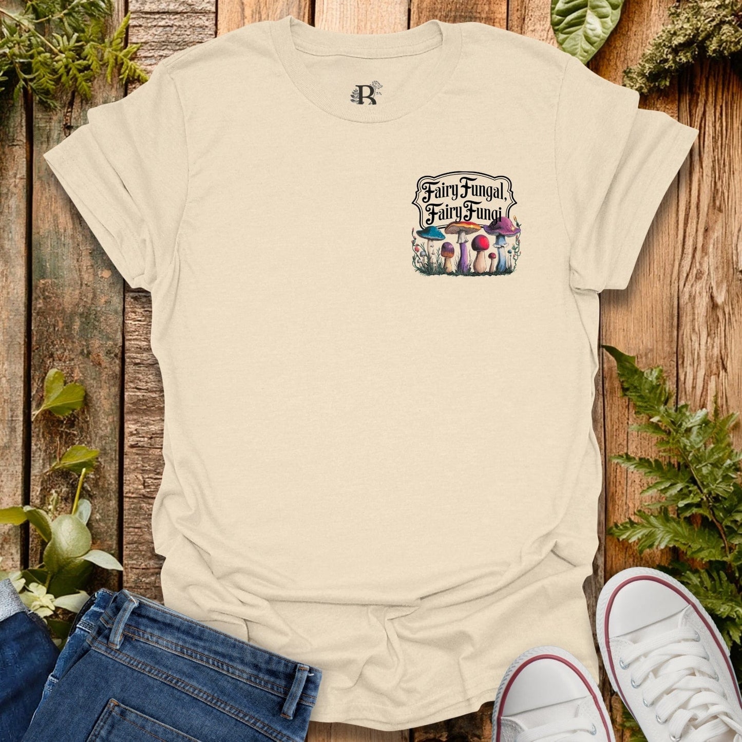 Beige t-shirt with 'Fairy Fungal' graphic on a wooden surface with plants.