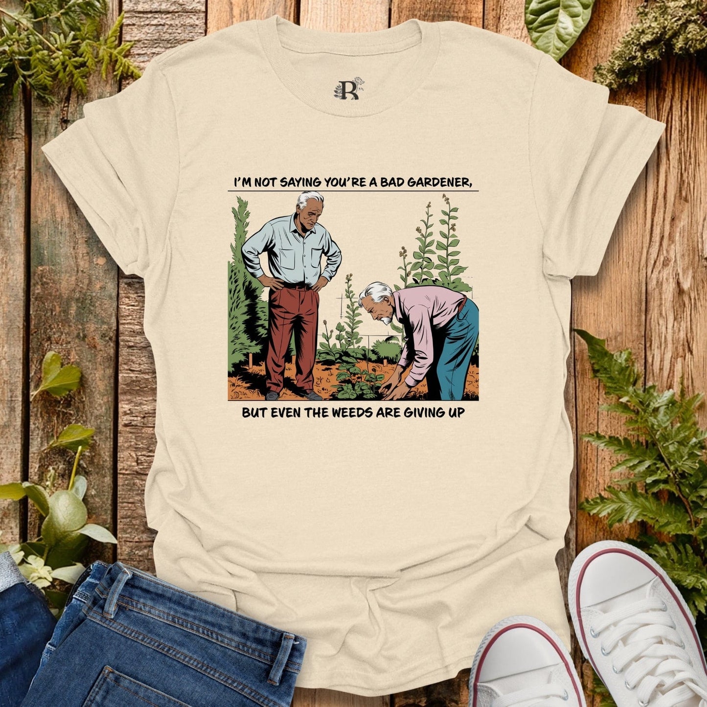 Beige t-shirt with a graphic of two men gardening and text on a wooden background.
