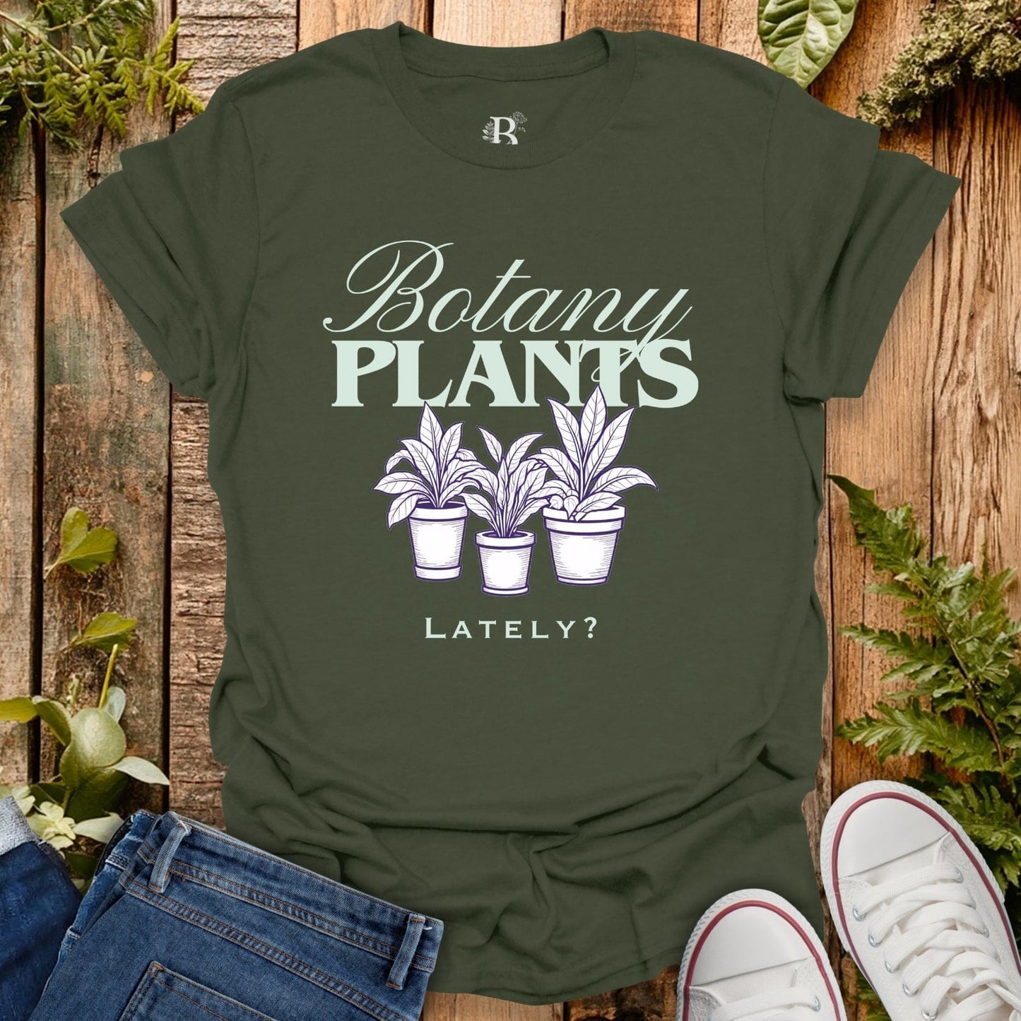 Green t-shirt with 'Botany Plants Lately?' design on a wooden background with plants.