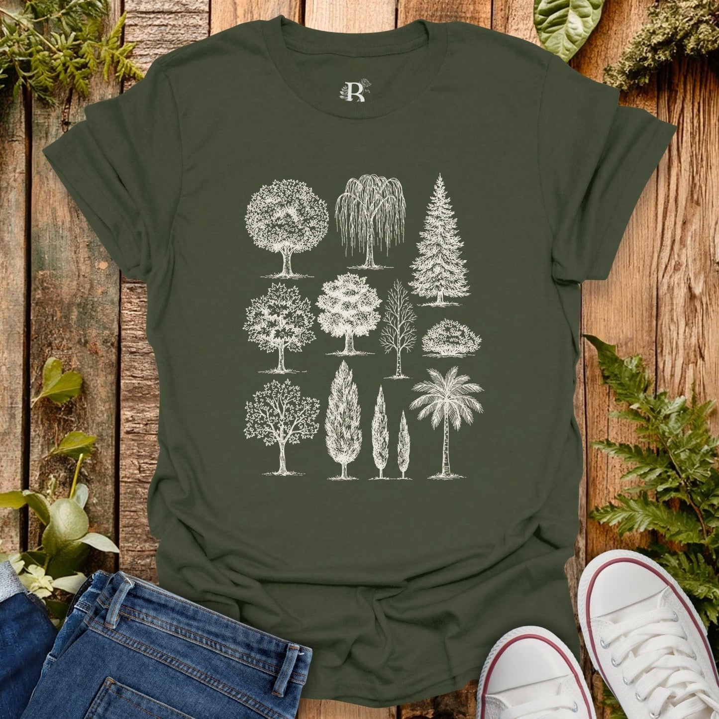 Green t-shirt with tree illustrations on a wooden surface with plants around